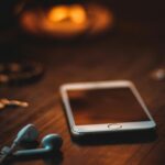 Mobile phone with earphones on a wooden table in warm ambient light, creating a cozy atmosphere.