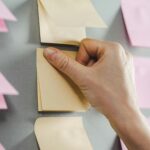 Close-up of a hand placing sticky notes on a wall, ideal for productivity concepts.